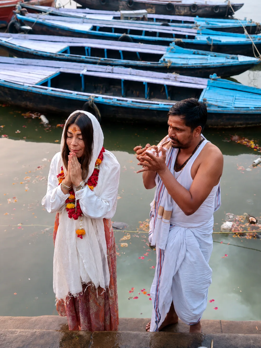 Traveller joining a respectful riverside ritual beside moored wooden boats in Varanasi