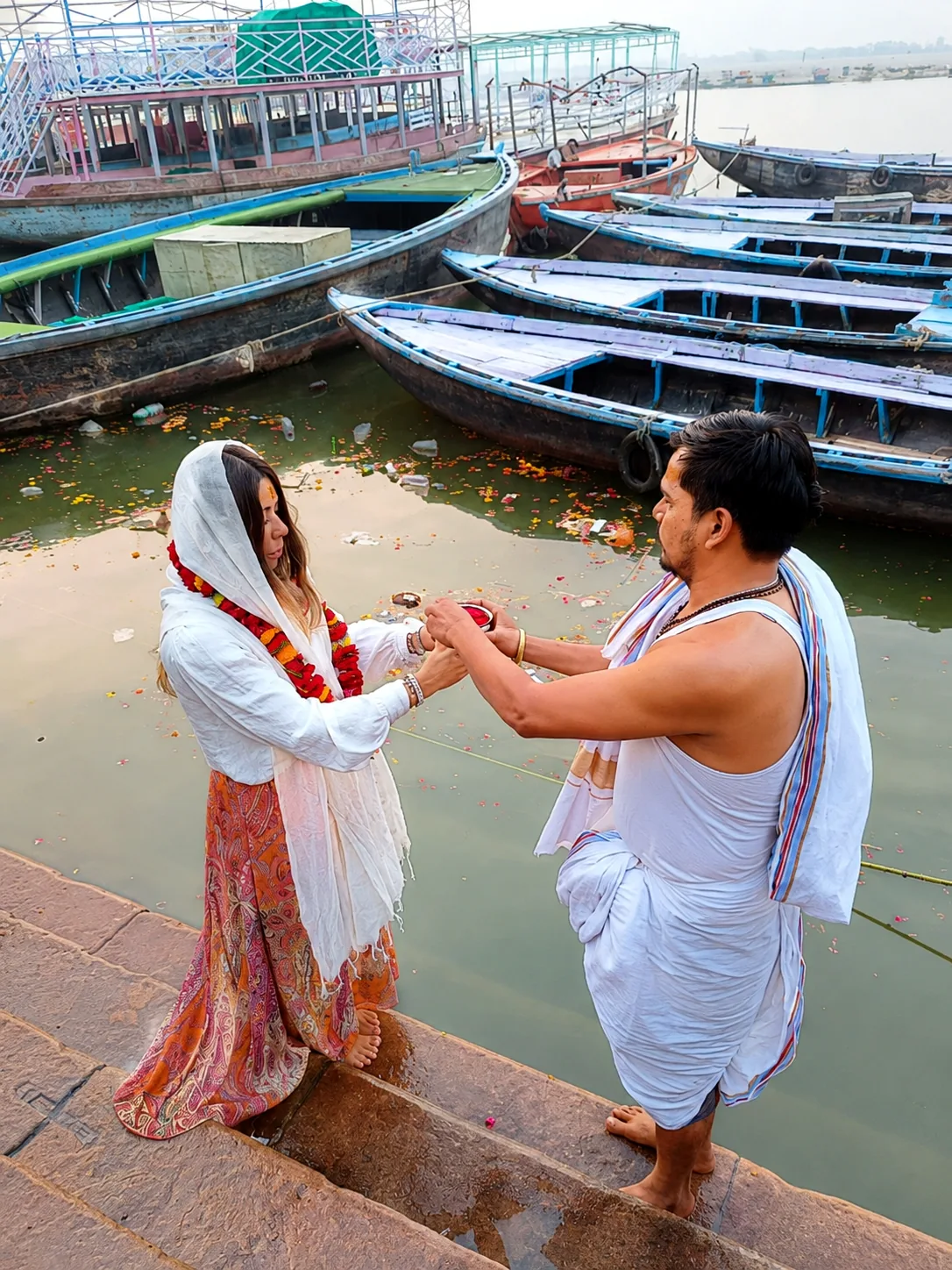 Traveller participating in a small riverside ritual beside wooden boats in Varanasi